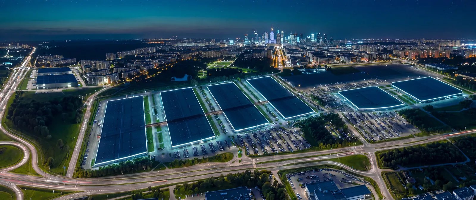 Widok z góry na Ptak Warsaw Expo nocą, w tle panorama Warszawy